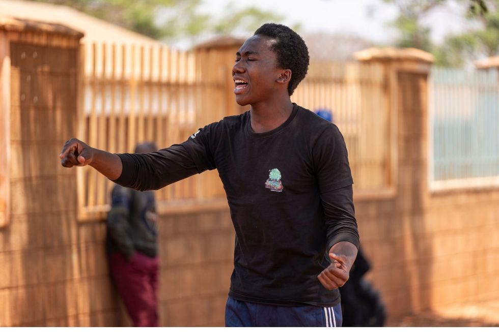 Espoir Kahitani interprétant passionnément la poésie parlée à l'extérieur, portant une chemise noire