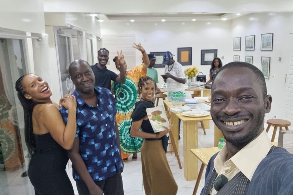 Une photo de selfie avec des gens souriant vivement derrière un fond blanc rempli d'œuvres d'art.