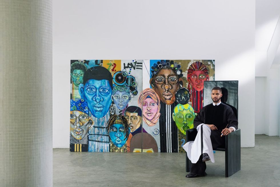 Osoranna est assise sur une chaise en bois noir, ses peintures en arrière-plan.