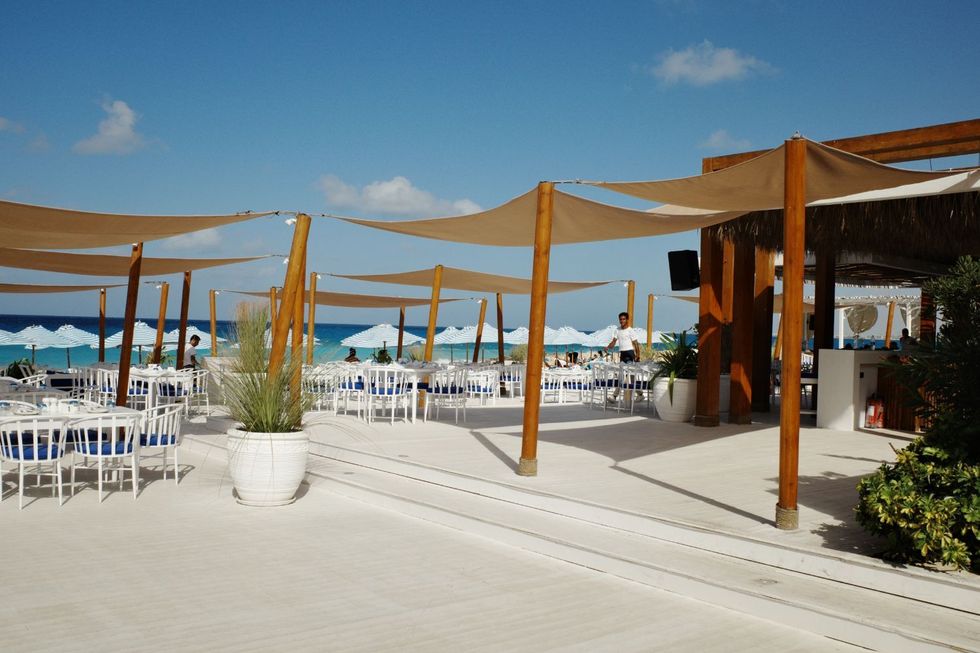 Un restaurant de la mer Méditerranée bleue avec des chaises blanches, des coussins bleus et de larges voiles de soleil.