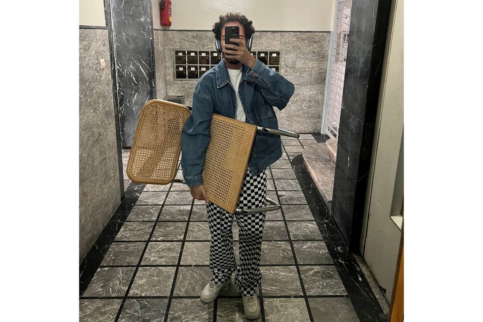 Youssef Oneechen porte une chaise et prend un selfie dans le miroir d'une entrée du bâtiment.