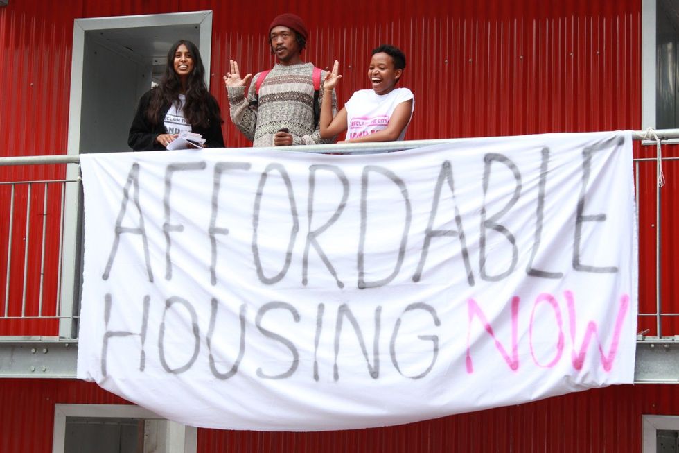 Un jeune homme et deux jeunes femmes se tiennent devant une bannière avec l'inscription "Housing abordable maintenant"
