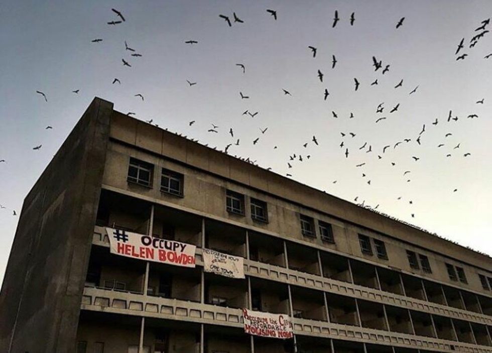 Un bâtiment non peint de trois étages avec des bannières qui lisent #occupyhelenbowden
