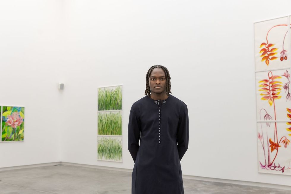 Kwaame Mintah pose pour une photo dans une tenue en deux pièces tout en se tenant derrière une série d'œuvres d'art.