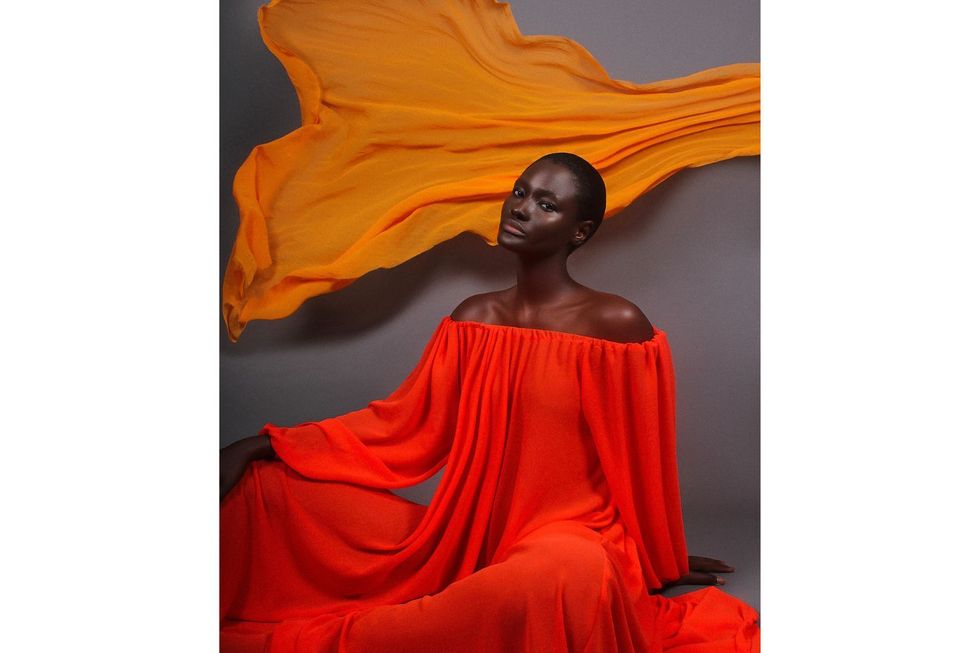 Modèle dans une robe de corail fluide avec un tissu orange derrière elle