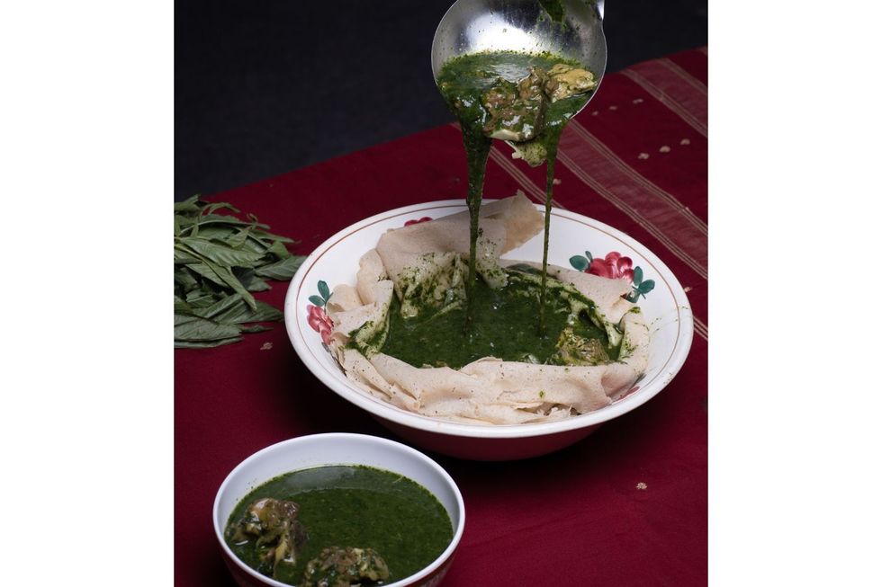 Une assiette blanche avec du pain kisra et de la molokhia avec de la viande dans un bol supplémentaire. Le Molokhia est versé sur le Kisra.