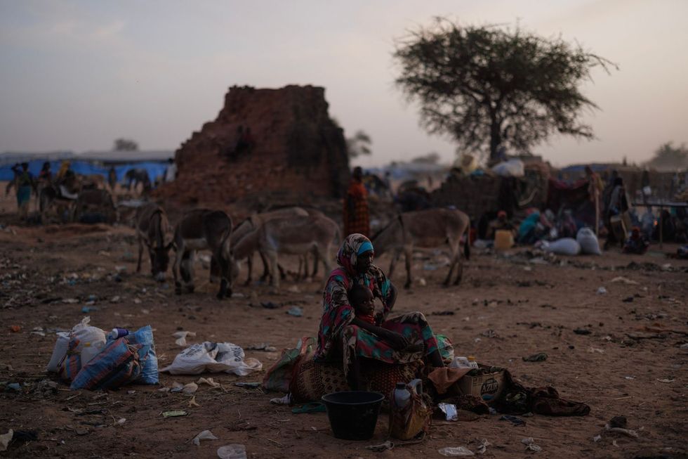 Une femme tient un jeune enfant au milieu d'un espace désertique occupée et poussiéreux qui est également bondé d'autres personnes et ânes.