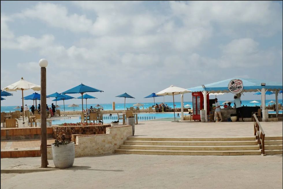 Une piscine près de la mer Méditerranée bleue avec des parapluies bleus et bleus et un kiosque de piscine appelé "Elsafwa".