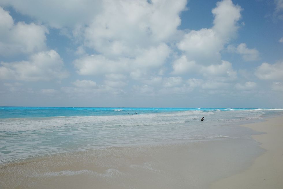 Une plage de sable blanc avec des vagues bleues; Quelques personnes sont dans l'eau au loin.