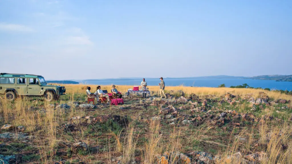 Rubondo Island Camp, lac Victoria, invités prenant un apéritif avec un véhicule derrière eux, lac devant