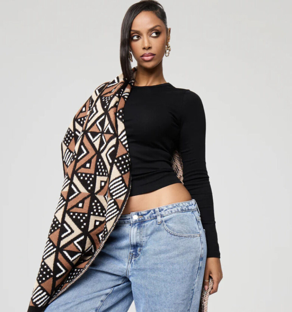 Restez au chaud dans cette écharpe pendant les mois froids. Un mannequin pose dans une écharpe à motif en toile de boue drapée sur une épaule.