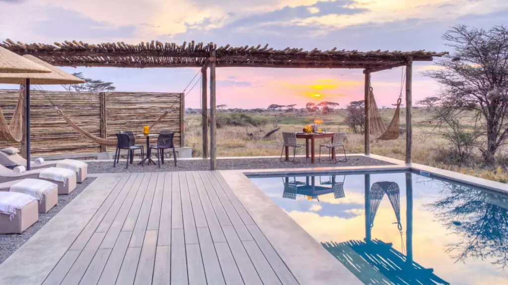 Plaines de Namiri, parc national du Serengeti, piscine au coucher du soleil, transats sur le pont, table et chaises, hamac