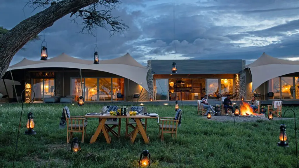 Les clients profitent d'un repas du soir en plein air et d'un feu de camp au Namiri Retreats avec des lanternes allumées, des tentes en toile illuminées et des nuages spectaculaires au-dessus.