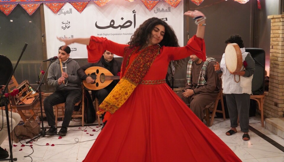 Un homme et une femme sont assis sur des chaises et tiennent des microphones. Elle rit, il chante. A côté de lui, une petite femme le regarde avec admiration tandis qu'un derviche virevolte devant eux.