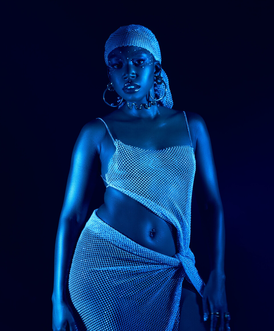 Portrait en studio éclairé en bleu de Karun portant un foulard en maille scintillante et une tenue deux pièces assortie.