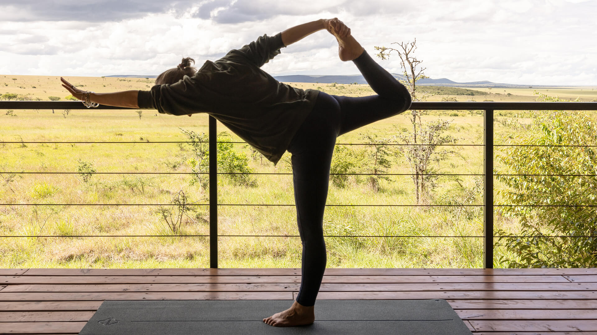 Invité pratiquant le yoga sur une terrasse en bois surplombant la savane au camp Naboisho.