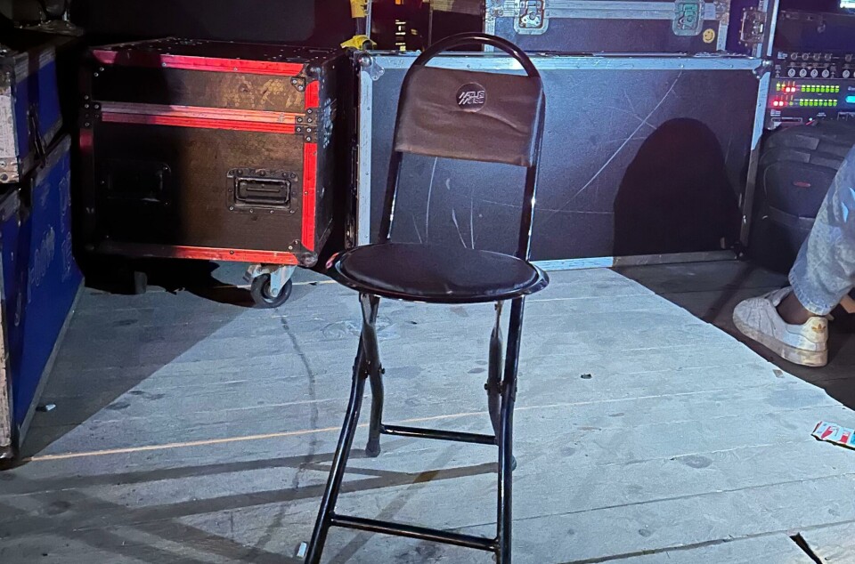 Une simple chaise noire avec un autocollant « Nazli's Noise » se tient dans les coulisses à côté du matériel d'ingénierie du son.