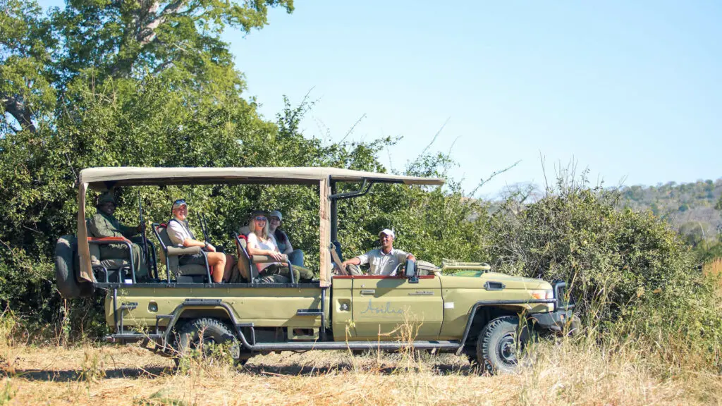 Maison privée Jabali, parc national de Ruaha, activité, invités participant à un jeu dans le véhicule avec des arbres en arrière-plan