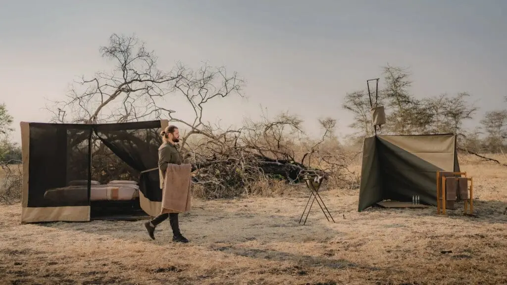 Une installation de camping à la mouche du camp Usangu avec un lit étoilé et un seau de douche dans le parc national de Ruaha