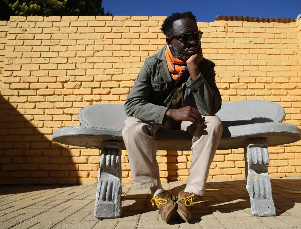 Un portrait de Bongani Madondo. Il est assis sur une chaise et pose son visage sur une main.