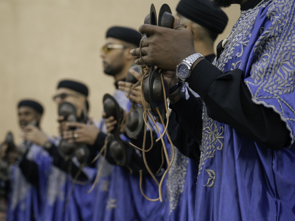 Une file de musiciens Gnaoua en tenue traditionnelle bleue clique sur leur qraqeb.