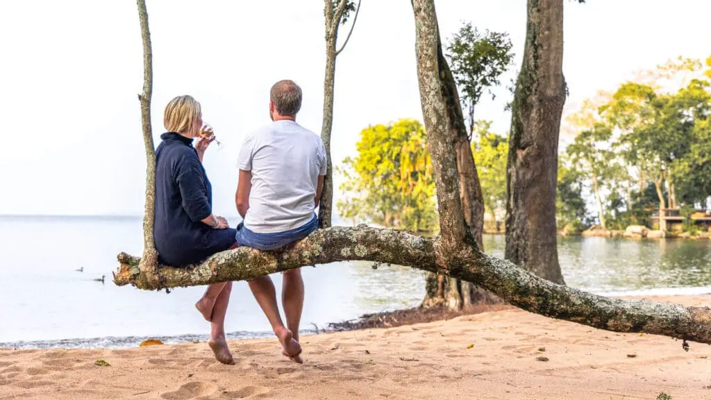 Un couple profite d'un apéritif assis sur une branche sur la plage du camp de l'île de Rubondo en Tanzanie - Asilia Africa