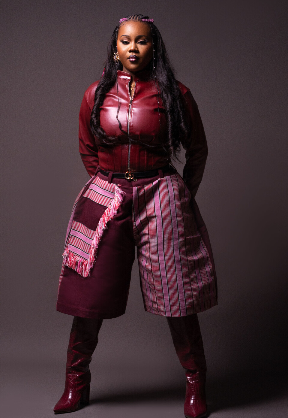 Portrait en studio d'un mannequin portant des pièces de mode bordeaux sur fond sombre.