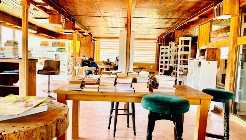 Espace intérieur rustique avec tables, tabourets, étagères en bois et lumière chaude du soleil.