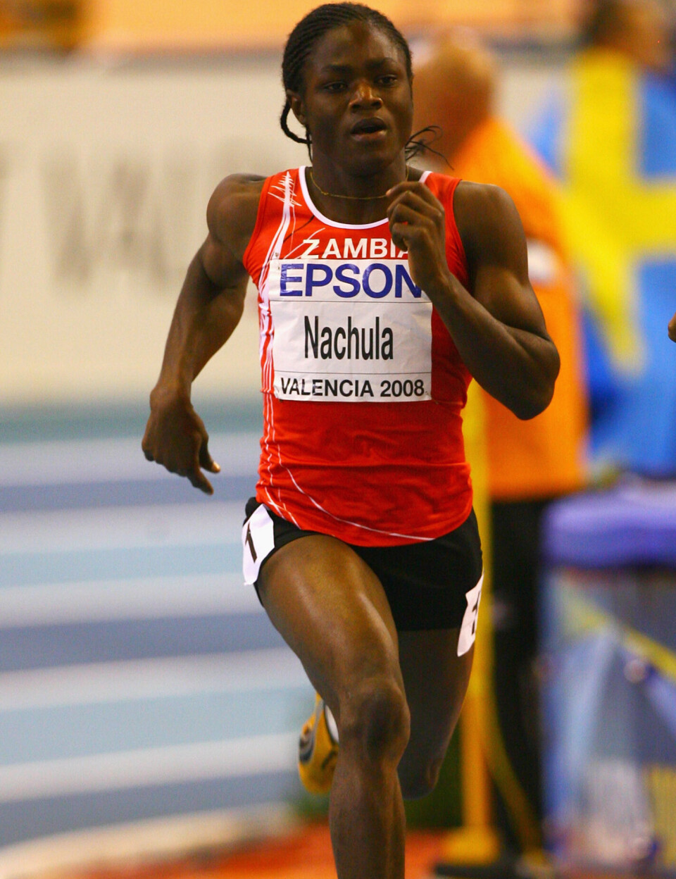 La coureuse zambienne Racheal Nachula sprinte en salle, vêtue d'un maillot rouge de la Zambie et d'un dossard numéro 8.