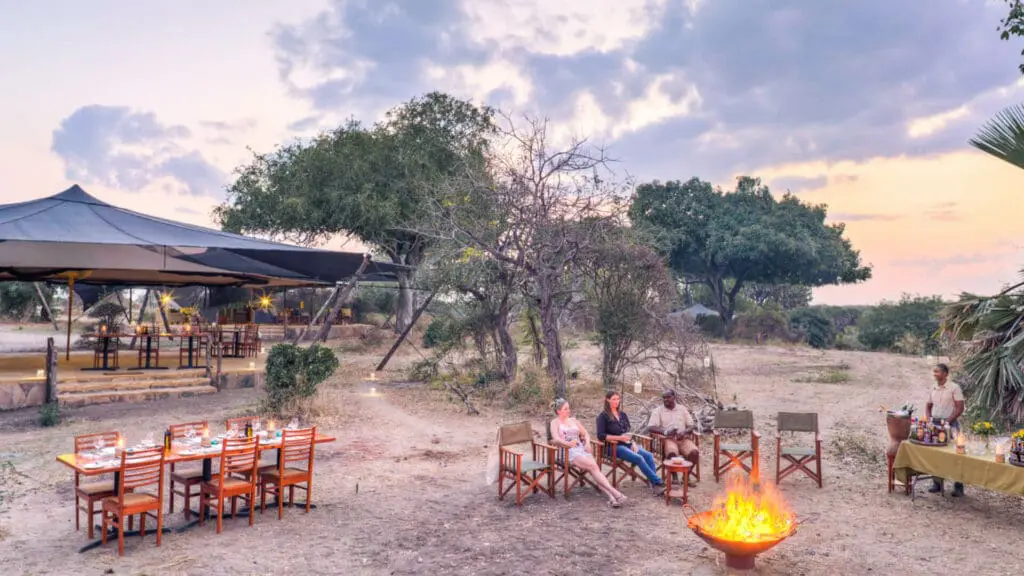 Camp Roho ya Selous, parc national de Nyerere, invités au foyer prenant un apéritif au coucher du soleil, dîner près de la zone principale
