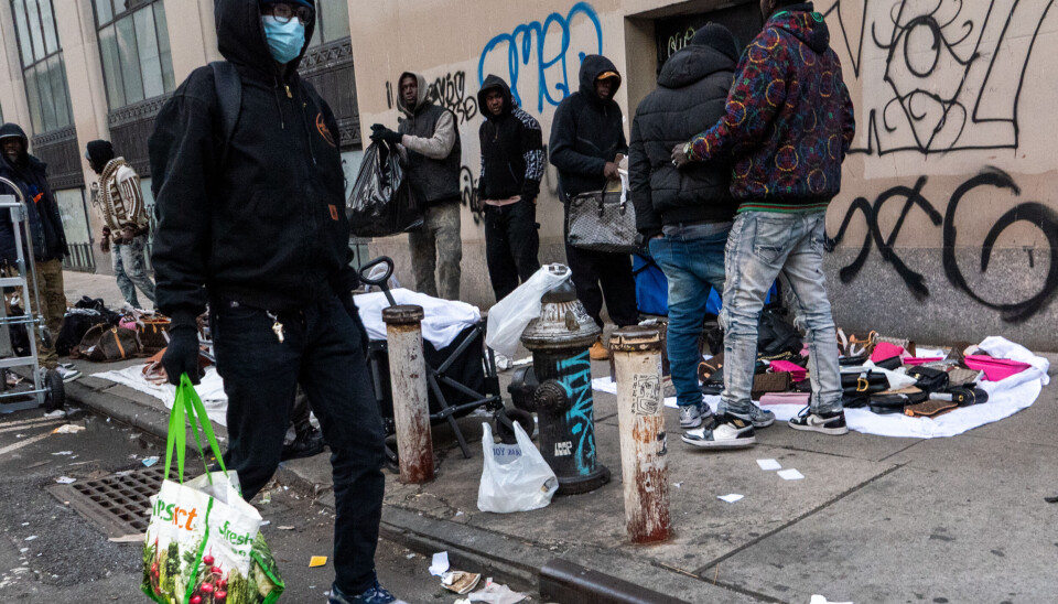 Des vendeurs ambulants exposent des sacs, des montres et des bijoux sur un trottoir new-yorkais bordé de graffitis.
