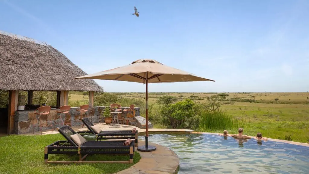 Les clients profitent de la piscine du Naboisho Camp, avec des chaises longues, des sièges ombragés et une grande savane s'étendant au loin sous un ciel dégagé.
