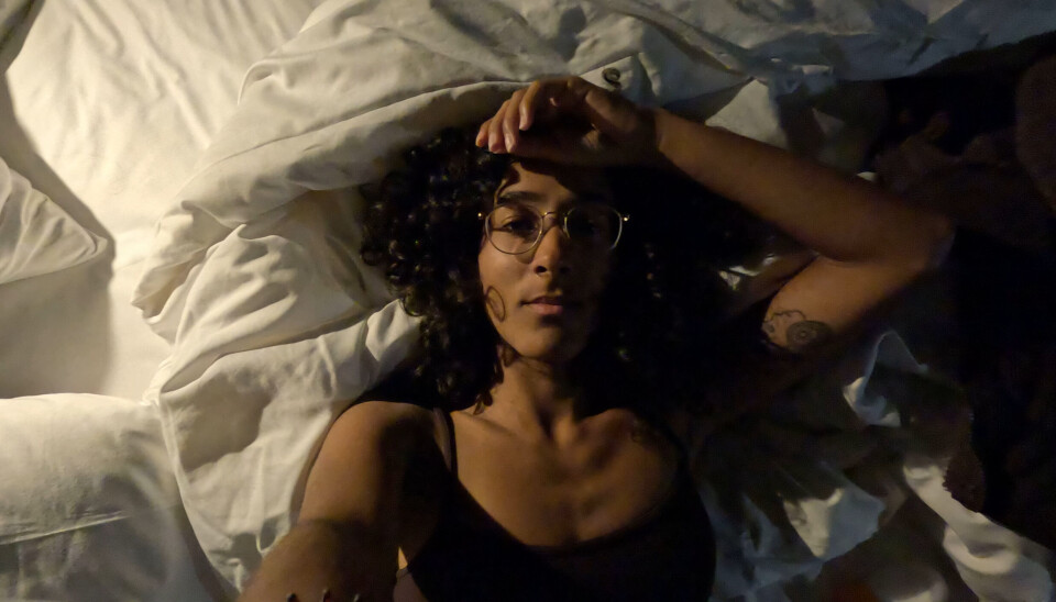 Une femme est allongée dans son lit et regarde la caméra avec un visage très fatigué.