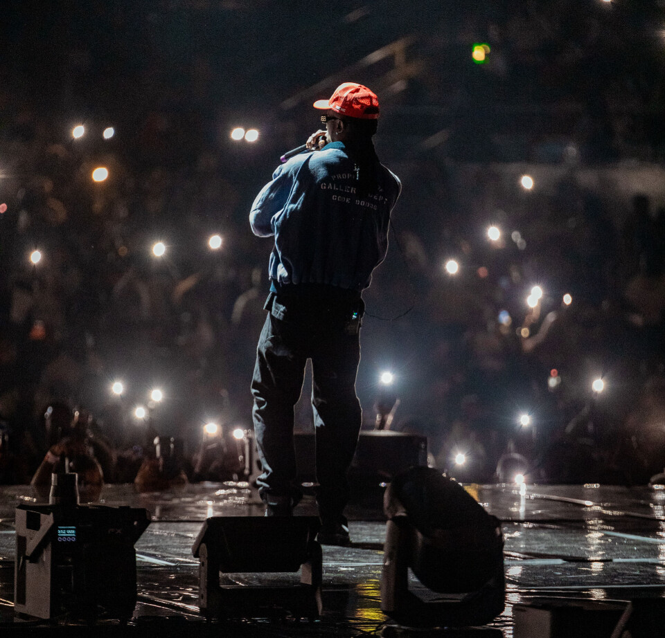 Vue arrière d'un artiste portant une casquette rouge face à une foule éclairée par les lumières du téléphone.